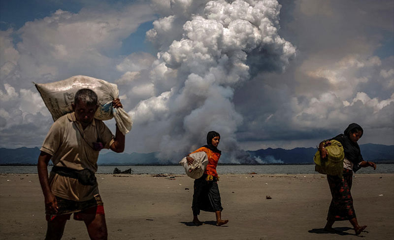 Smoke is seen on the Myanmar border as Rohingya refugees walk on the shore after crossing the Bangladesh-Myanmar border by boat through the Bay of Bengal, in Shah Porir Dwip, Bangladesh September 11, 2017. REUTERS/Danish Siddiqui