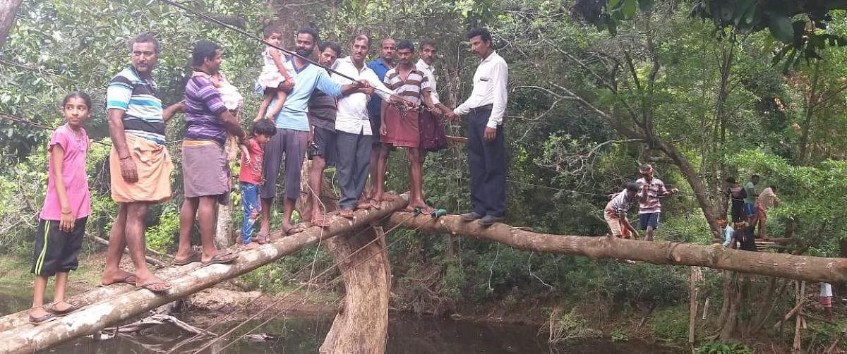 Villagers balance on hanging bridge to cross rivulet