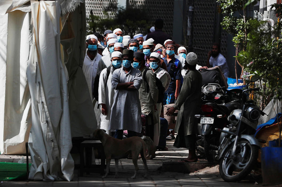 Men wearing protective masks wait for a bus that will take them to a quarantine facility, amid concerns about the spread of coronavirus disease (COVID-19), in Nizamuddin area of New Delhi. (Reuters Photo)