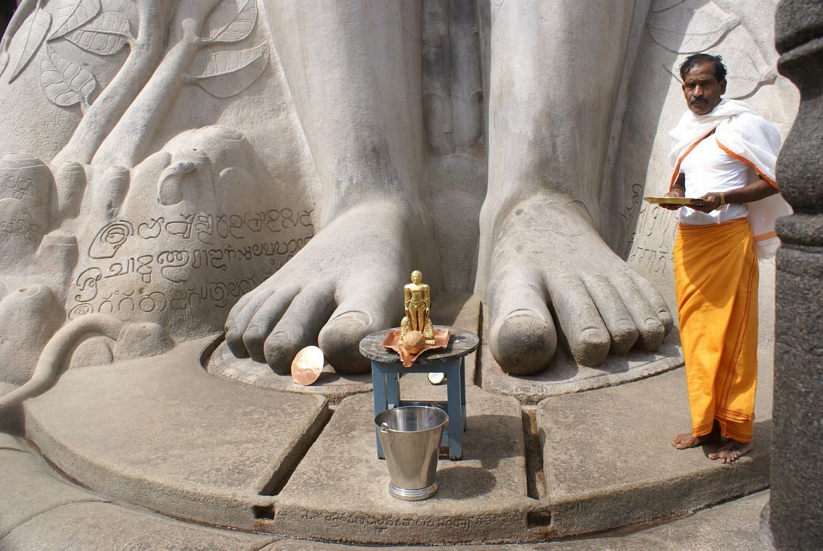 The legs of Bahubali dwarf the priest