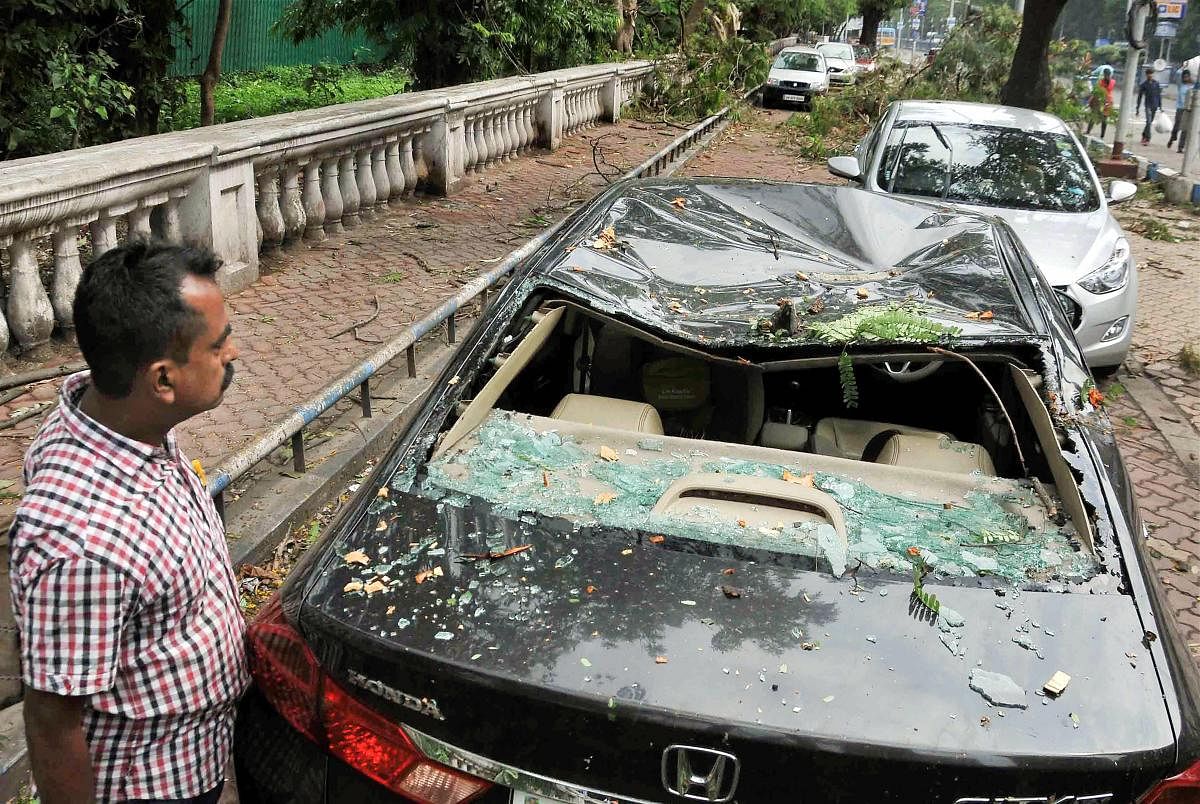 A man inspects a damaged car after heavy storm and rain in Kolkata on Wednesday. More than eight people were killed and several others injured on Tuesday after strong winds of up to 98 km per hour hit the West Bengal capital and its adjoining areas, disrupting public transport and traffic. PTI