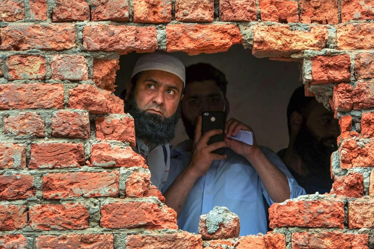 A man looking out from a hole of a house which was damaged during encounter between security forces and militants at Chatabal in Srinagar, on Saturday. Three militants and civilian were killed in the gunbattle. PTI