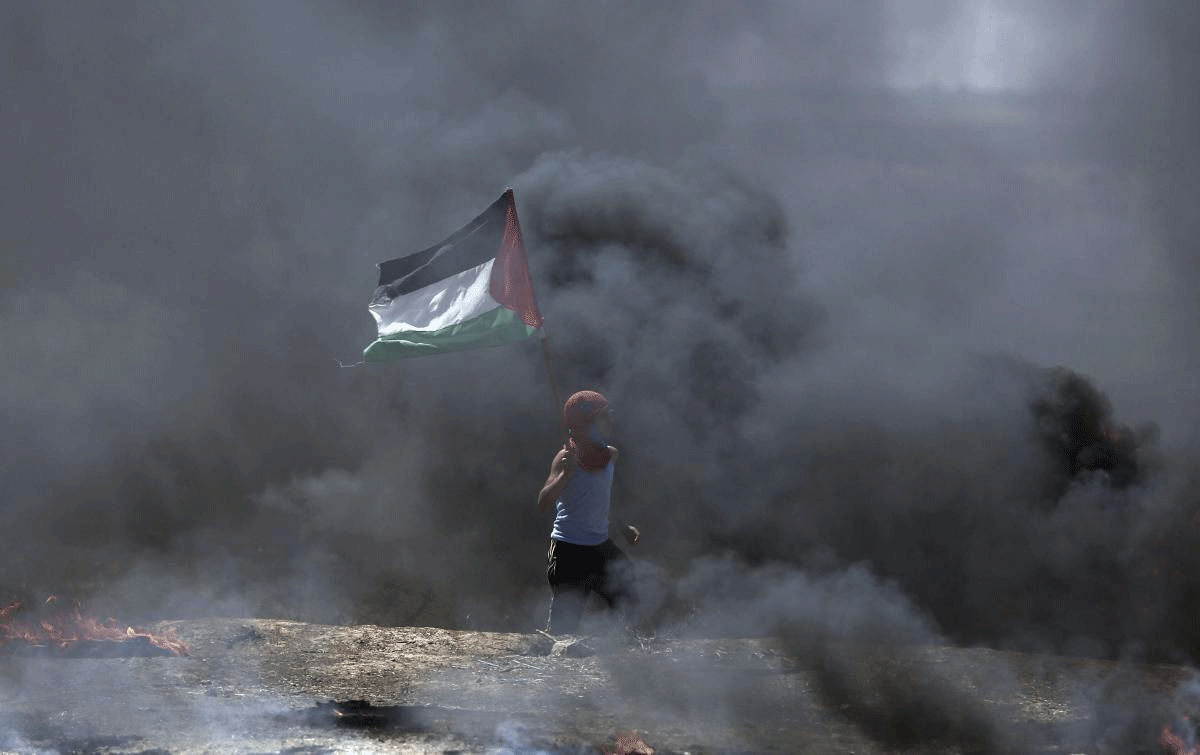 A boy waves a Palestinian flag while walking through black smoke from burning tires during a protest on the Gaza Strip's border with Israel, Monday, May 14, 2018. Thousands of Palestinians are protesting near Gaza's border with Israel, as Israel prepared for the festive inauguration of a new U.S. Embassy in contested Jerusalem. AP/PTI