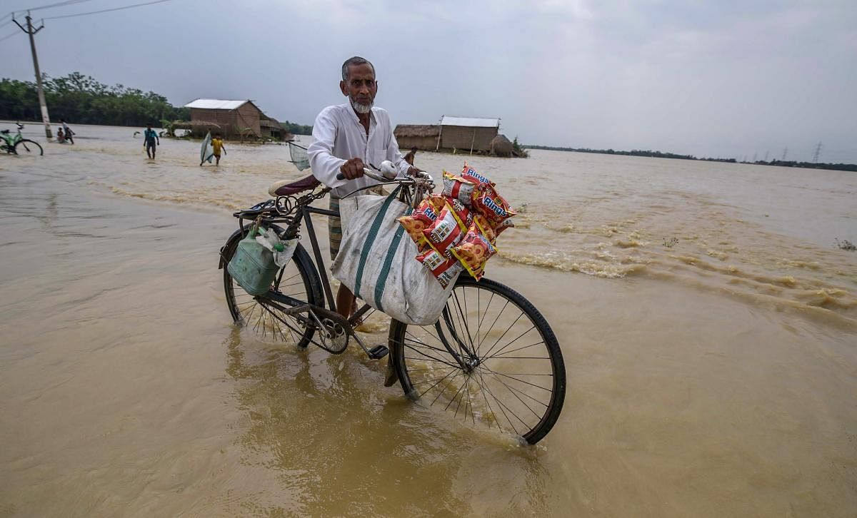 A man pushes his bicycle through flood water at Jamunamukh village in Hojai district of Assam. PTI Photo