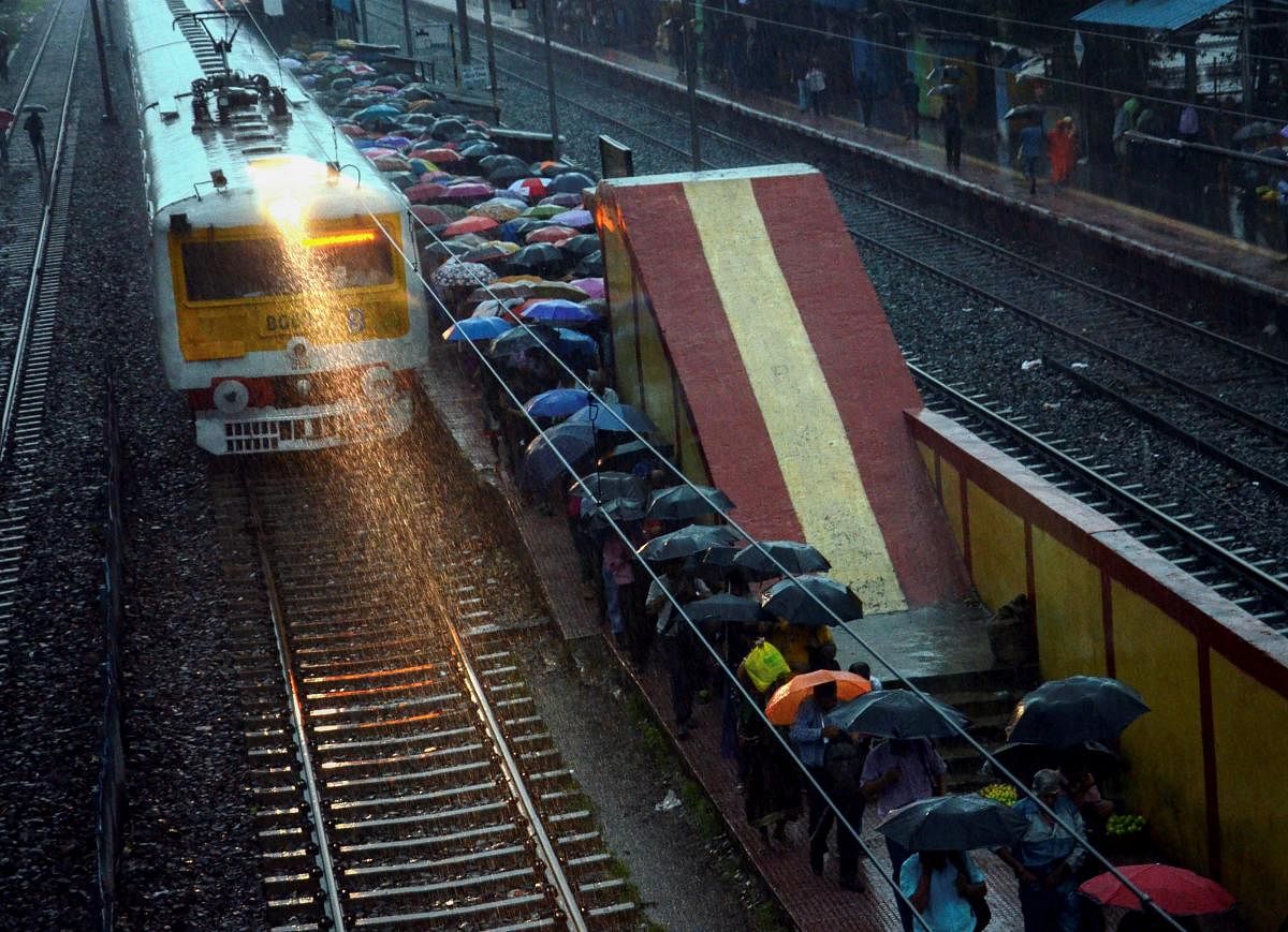 A local train makes way through heavy rains as passengers shield themselves under umbrella at a railway station, in Kolkata on Monday morning, June 25, 2018. PTI