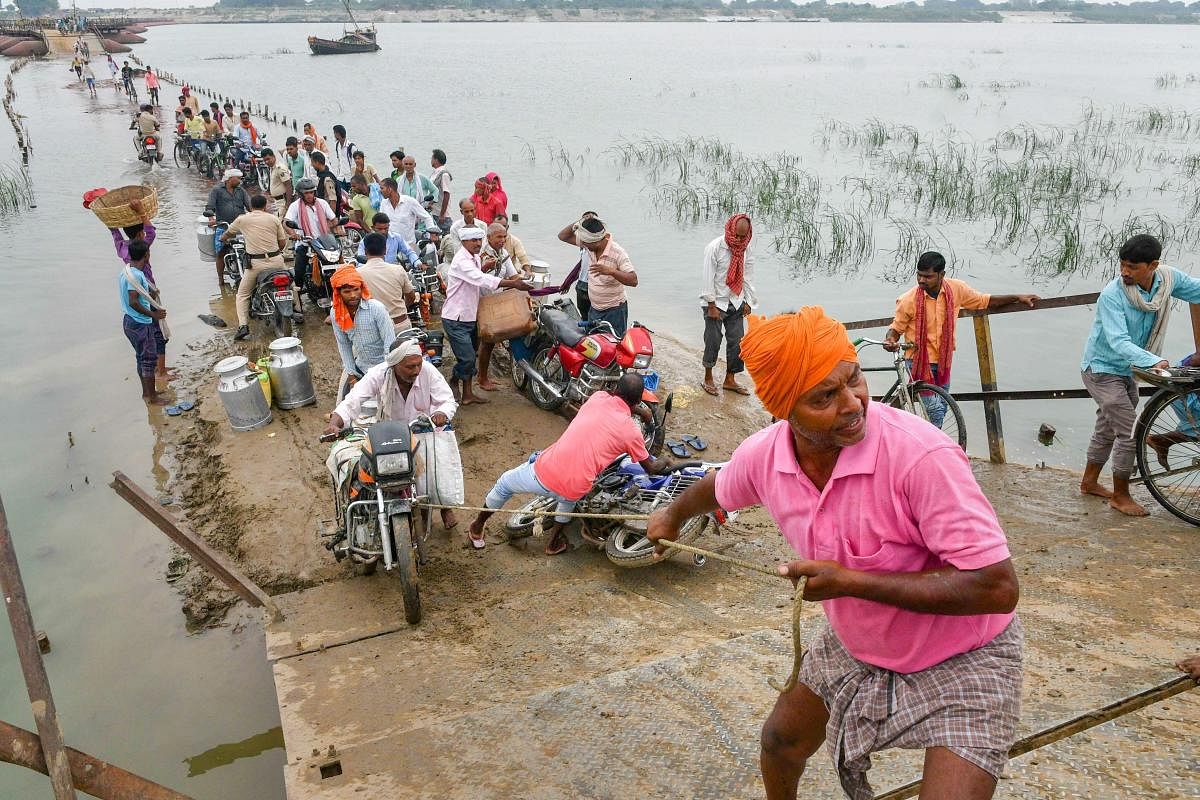 A man helps a biker wade through a flooded road after the water level of Ganga river increased, at Danapur in Patna on Monday, July 02, 2018. (PTI Photo)