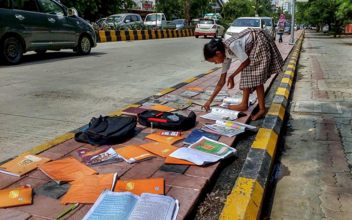 A girl dries up her school books on the pavement, after heavy rains, in Nagpur on Saturday, July 7, 2018. (PTI Photo)