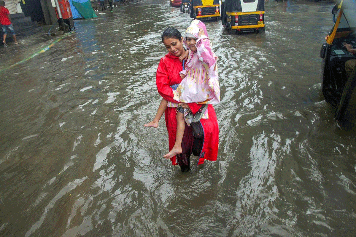 A woman, carrying a girl, wades through a waterlogged road during heavy rains, in Thane on Monday, July 9, 2018. (PTI Photo)