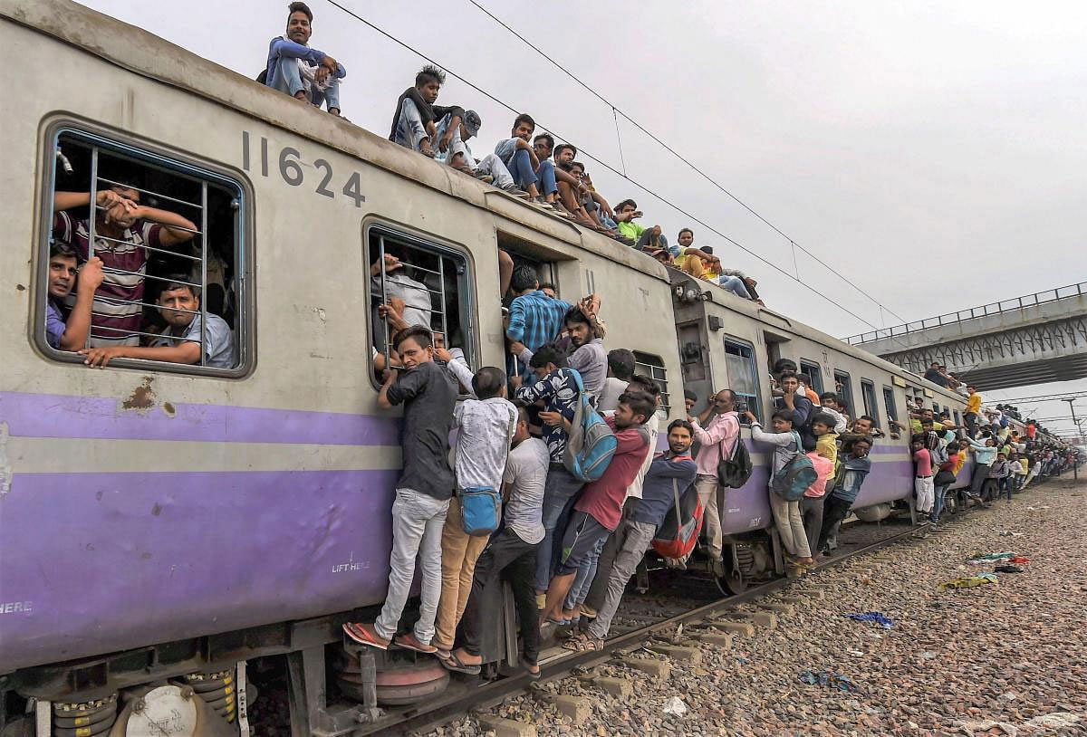 Commuters hang on the gates and sit on the roof while traveling by a crowded train on World Population Day, at Noli Railway Station near Ghaziabad on Wednesday, July 11, 2018. The theme of World Population Day 2018 is ''Family planning is a human right'. PTI Photo