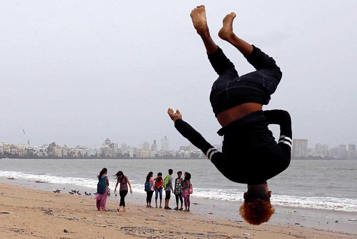 Beachgoers stroll as a boy practices somersaulting on a beach in Mumbai, India, July 12, 2018. REUTERS