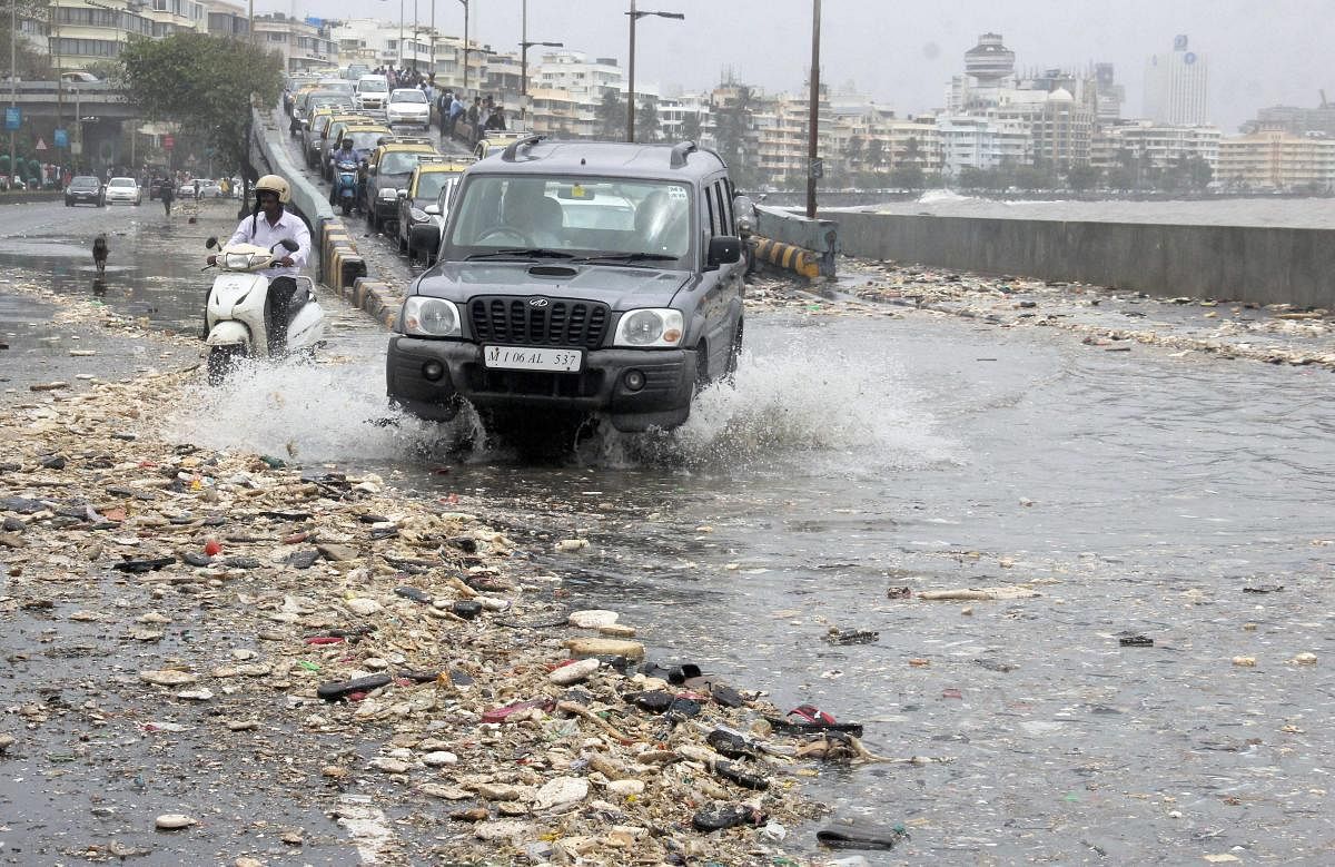 Commuters wade through a garbage-filled street washed ashore during high tide on a road along the Marine Drive in Mumbai on Saturday, July 14, 2018. (PTI Photo)