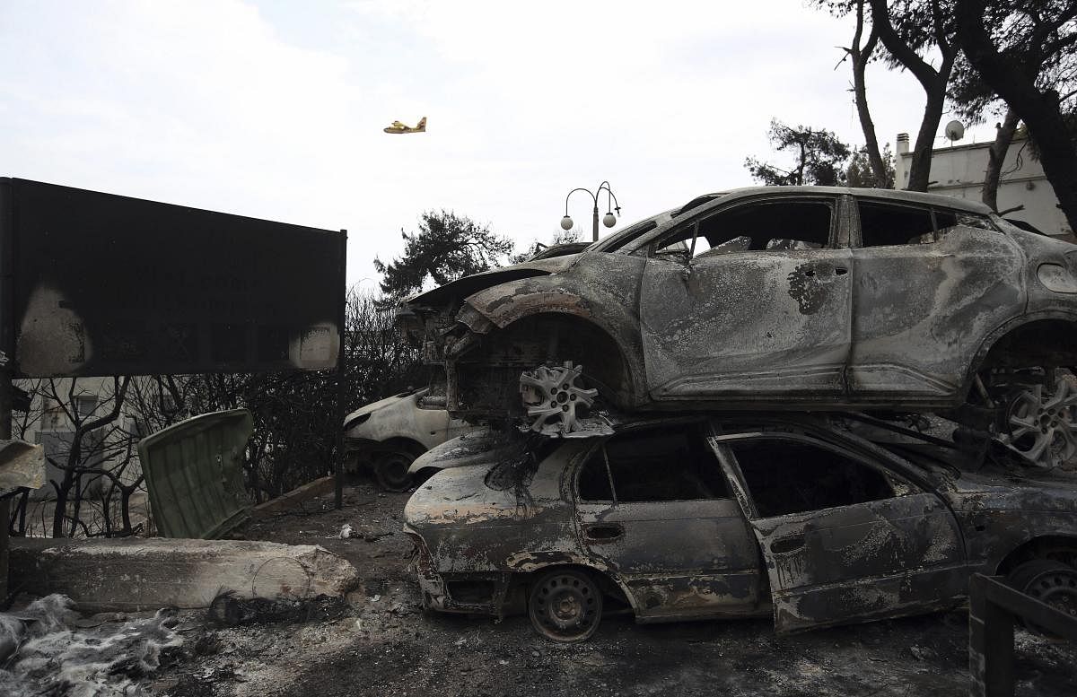 A firefighting plane flies above burned-out cars in Mati, east of Athens. Twin wildfires raging through popular seaside areas near the Greek capital have torched homes, cars and forests and killed at least 49 people. (AP/PTI Photo)