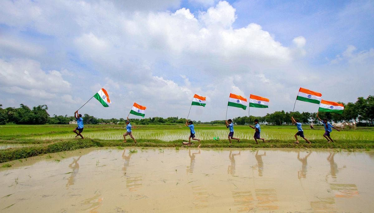 School children run across a paddy field with the tricolour, ahead of 72nd Independence Day celebrations, at Debagram in Birbhum on Monday, Aug 13, 2018. (PTI Photo)