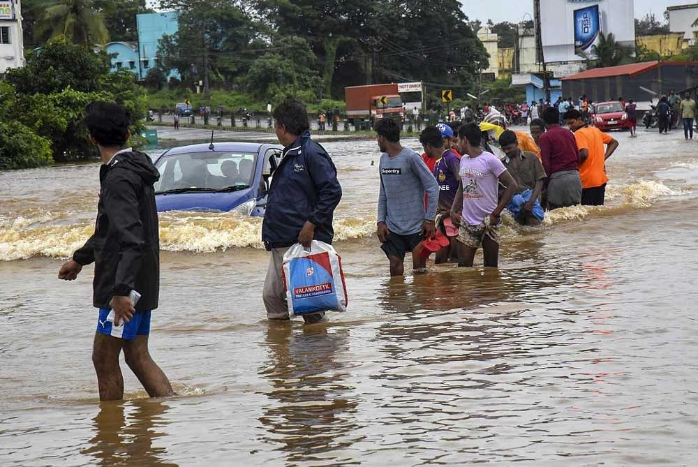 Pedestrians wade across waterlogged streets as heavy monsoon rains causes floods, in Kochi on Friday. PTI Photo