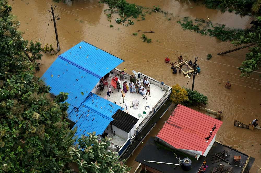 People wait for aid on the roof of their house at a flooded area in Kerala. Reuters Photo