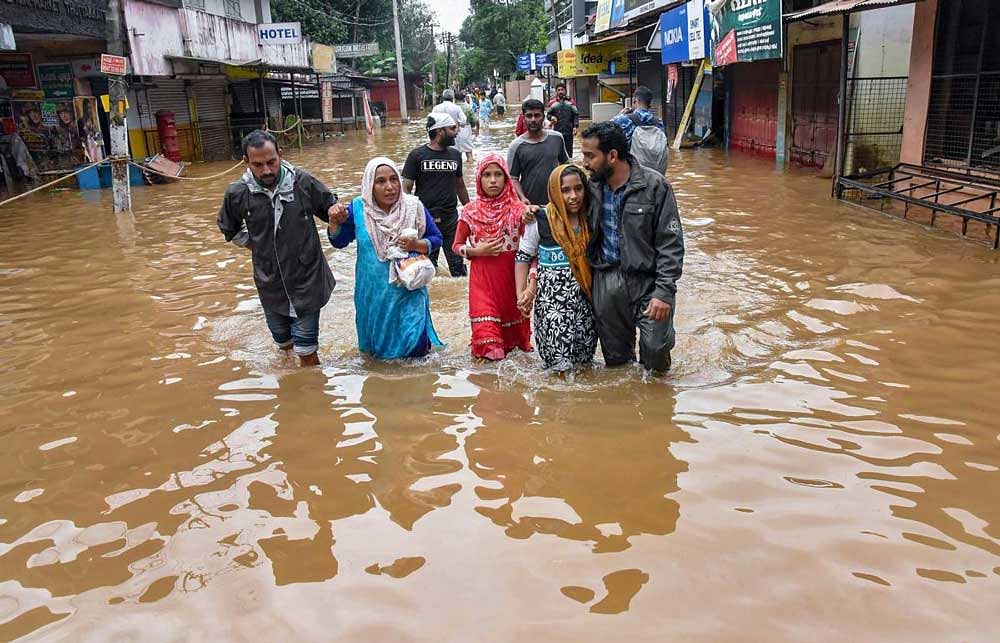 People wade across a waterlogged street after being rescued from flood-affected regions following heavy monsoon rainfall, in Kochi. PTI Photo
