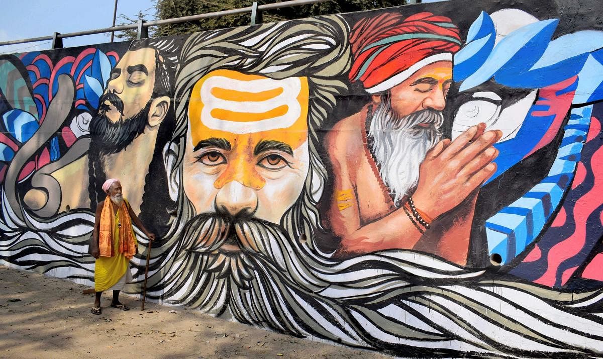 A sadhu walks past a mural painting created as a part of the ongoing project 'Paint my City' for the upcoming Kumbh Mela festival, in Allahabad, Tuesday, Oct 30, 2018. (PTI Photo)