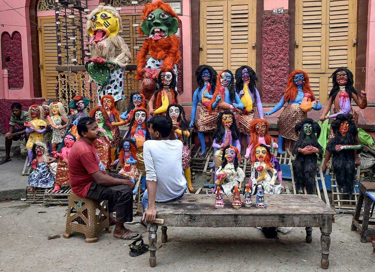 Vendors sit beside the mythological characters of demons made from clay, on the eve of 'Kali Puja', at an artisan village in Kolkata, Monday, November 05, 2018. PTI Photo