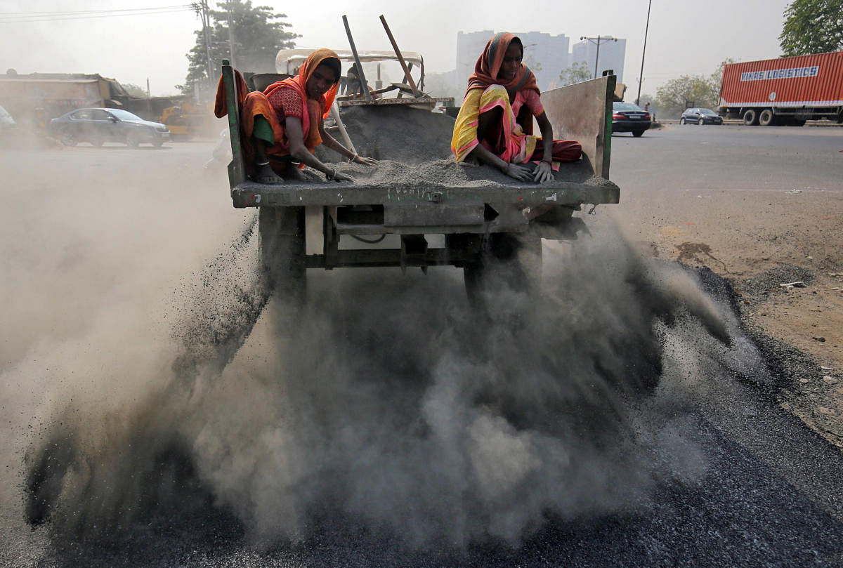 Labourers spread ash over newly constructed road tarmac to dry it and fill in the gaps, on the outskirts of Ahmedabad. (Reuters Photo)