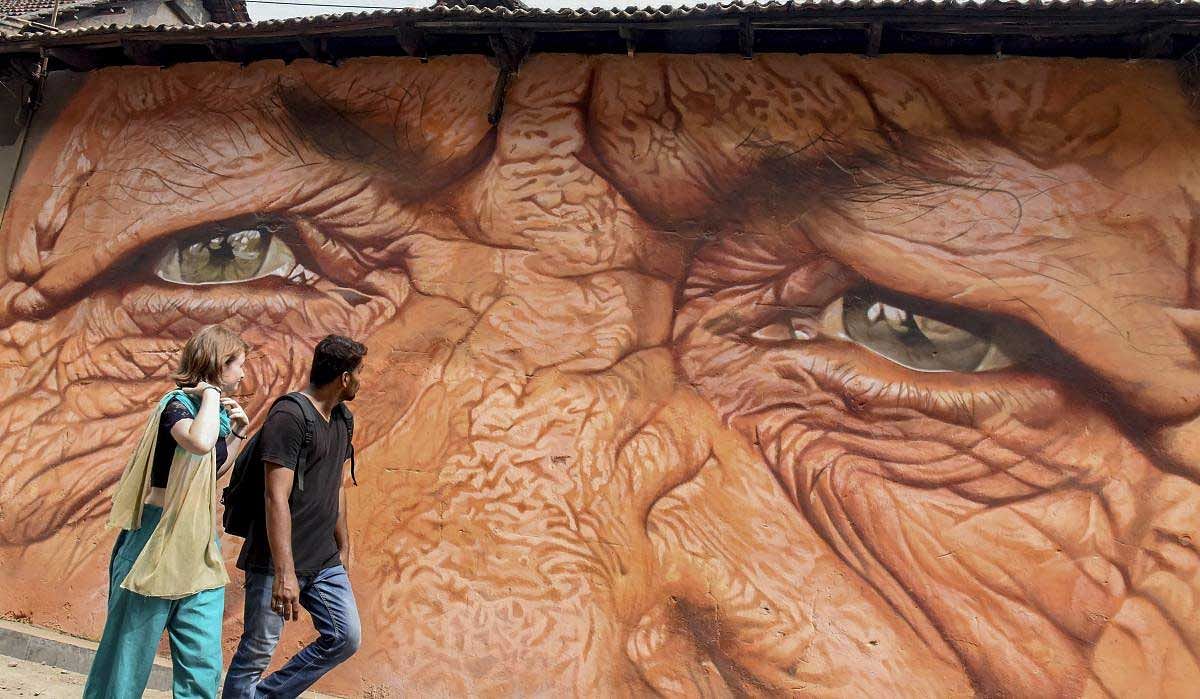 A couple walks past a painting on a wall which will be part of the 4th edition of 'Kochi Muziris Biennale', an international exhibition of contemporary art to be held on Dec.12th, in Kochi, Monday, Dec. 10, 2018. (PTI Photo)