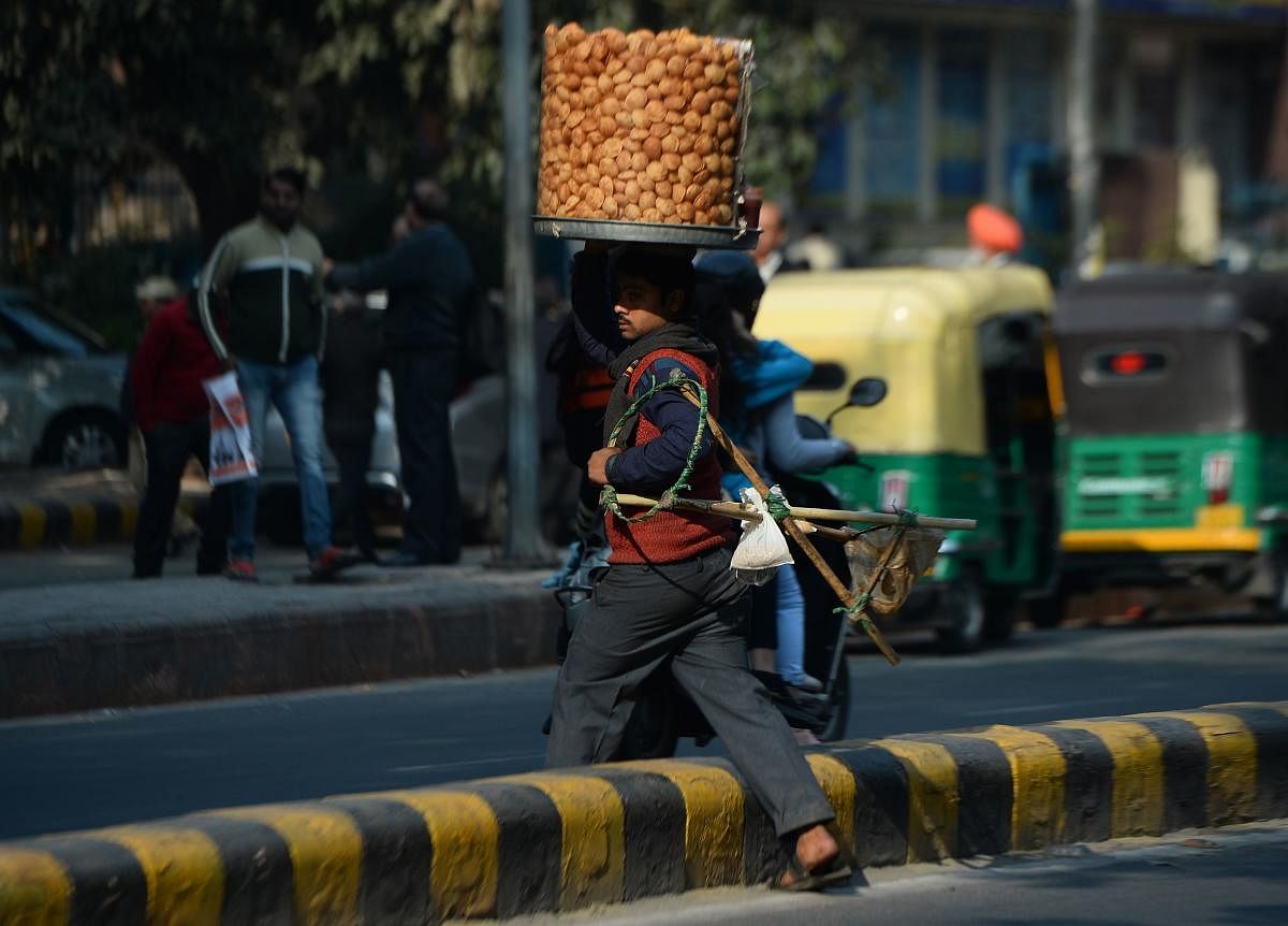 An Indian vendor carrying a container of golgappa snacks on his head crosses a road in New Delhi on December 20, 2018. (Photo by Sajjad HUSSAIN / AFP)