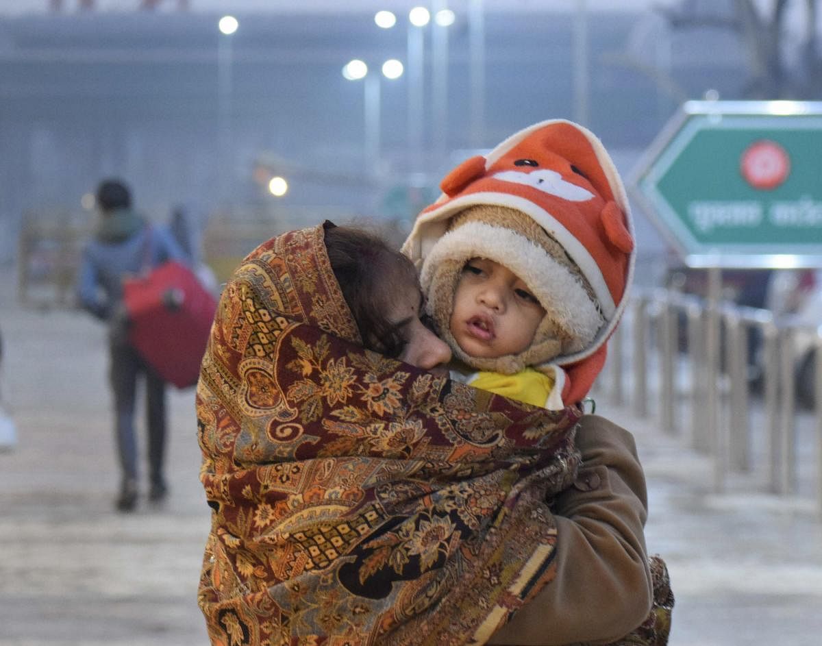 A child and mother wrapped in warm clothes wait at the station as trains run late on a cold, foggy winter morning, in Allahabad. PTI