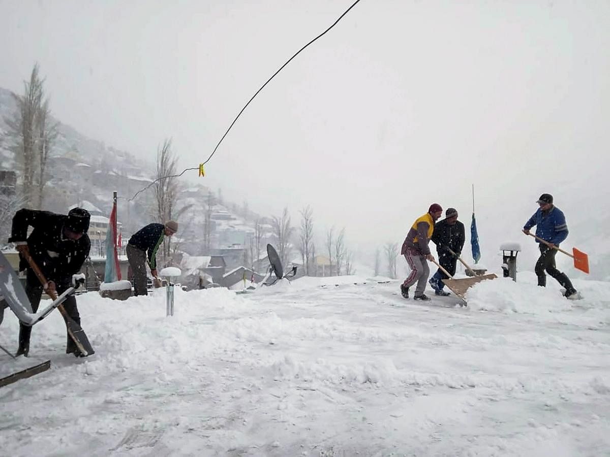 People clear snow outside their houses during fresh snowfall in Lahaul Spiti, Himachal Pradesh. (PTI Photo)