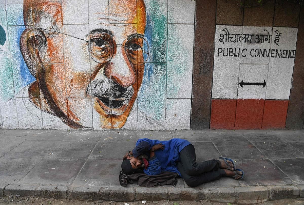 A man sleeps on the ground in front of a mural of Mahatma Gandhi in New Delhi on February 12, 2019. (Photo by Sajjad HUSSAIN / AFP)