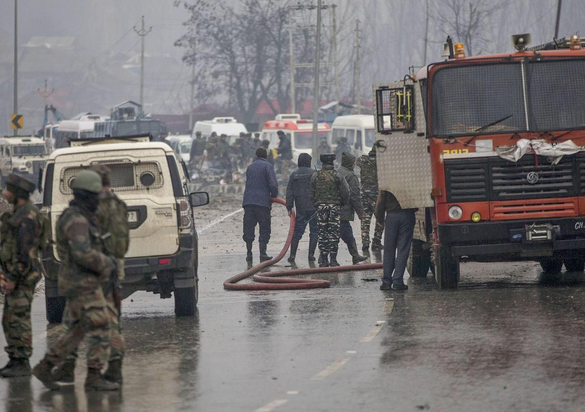 Firemen spray water on a road to wash away the blood stains at the site of suicide bomb attack at Lathepora Awantipora in Pulwama district of south Kashmir, Thursday, February 14, 2019. At least 30 CRPF jawans were killed and dozens other injured when a CRPF convoy was attacked. (PTI Photo)