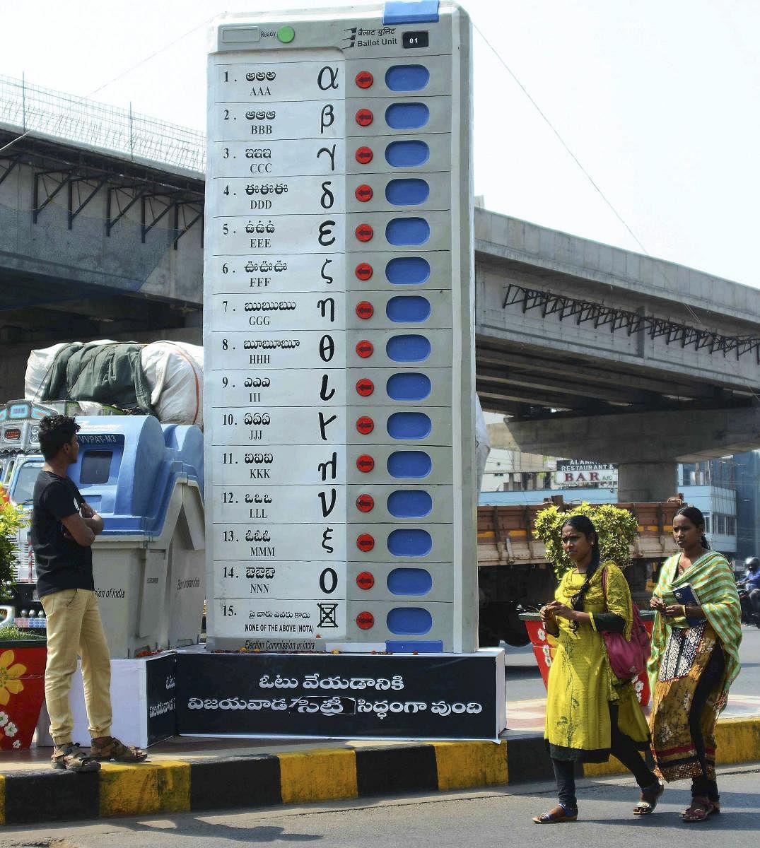 Pedestrians walk past a replica of Electronic Voting Machine (EVM) installed by the Election Commission of India to create awareness about voting at Benz circle, in Vijayawada. (PTI Photo)