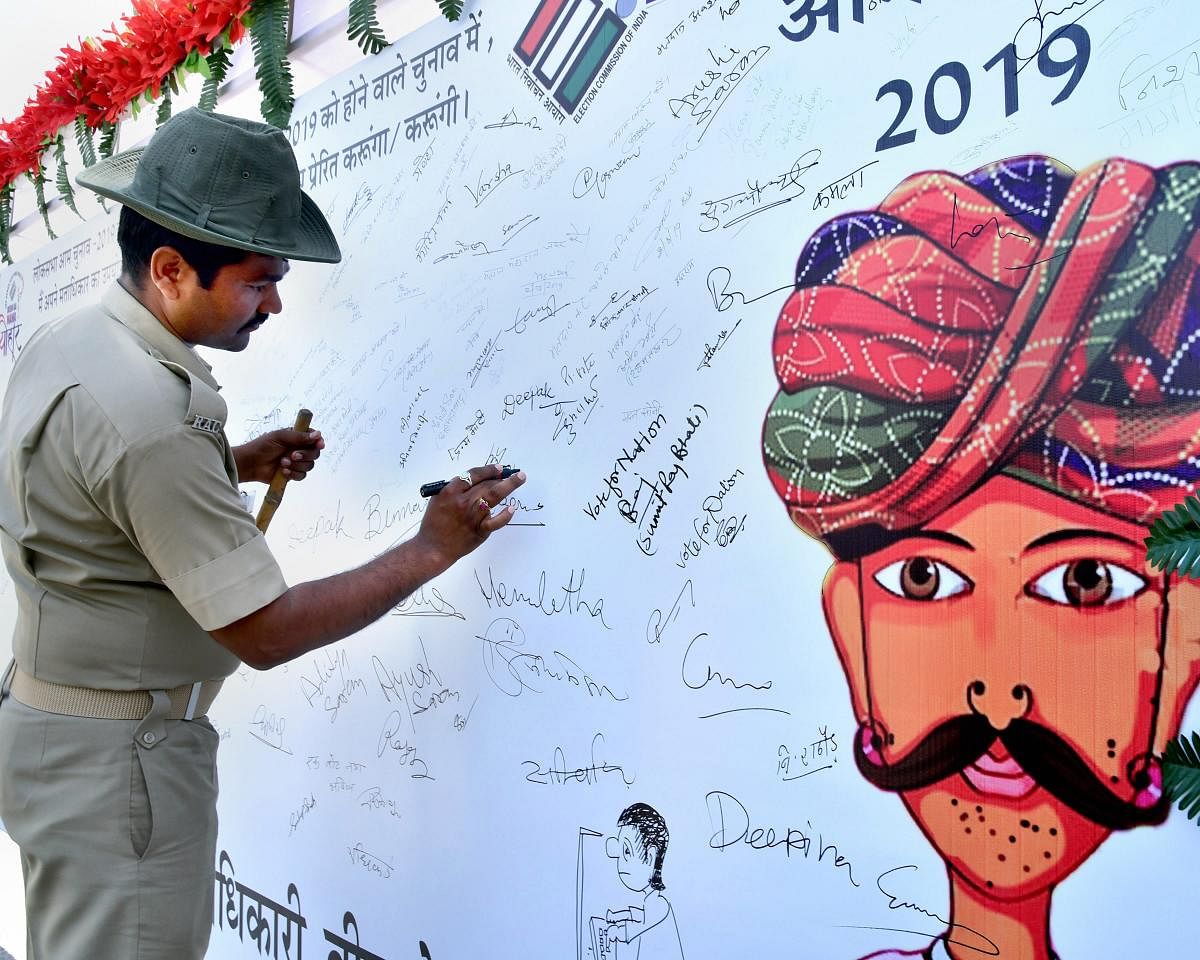 A Rajasthan Armed Constabulary (RAC) jawan puts his signature on a banner during an election awareness campaign, in Bikaner, Friday, April 05, 2019. (PTI Photo)