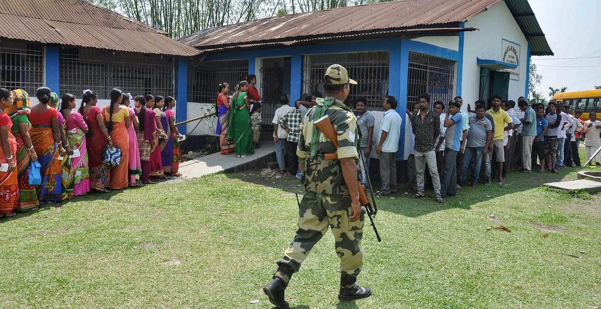 Siliguri: A security personnel stands guard as voters queue to cast their vote during the second phase of general elections, at a polling station, in Siliguri, Thursday, April 18, 2019. PTI