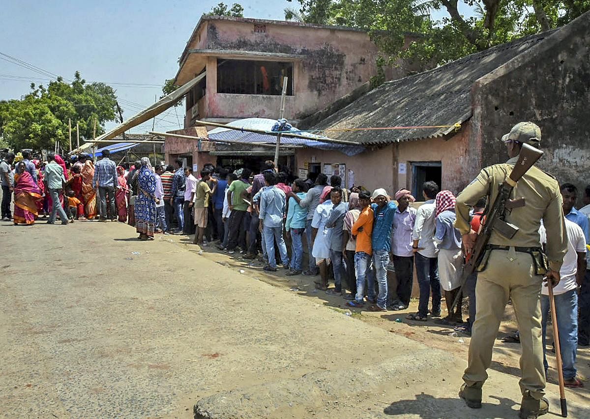 A security personnel stands guard as voters queue outside a polling station to cast their vote, during the 4th phase of Lok Sabha elections, at Mahakalapada in Kendrapara. (PTI Photo)