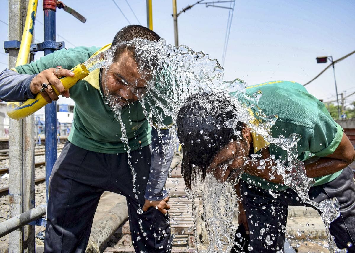 Passengers splash water over themselves on a hot, summer day at the railway station, in Prayagraj. (PTI Photo)