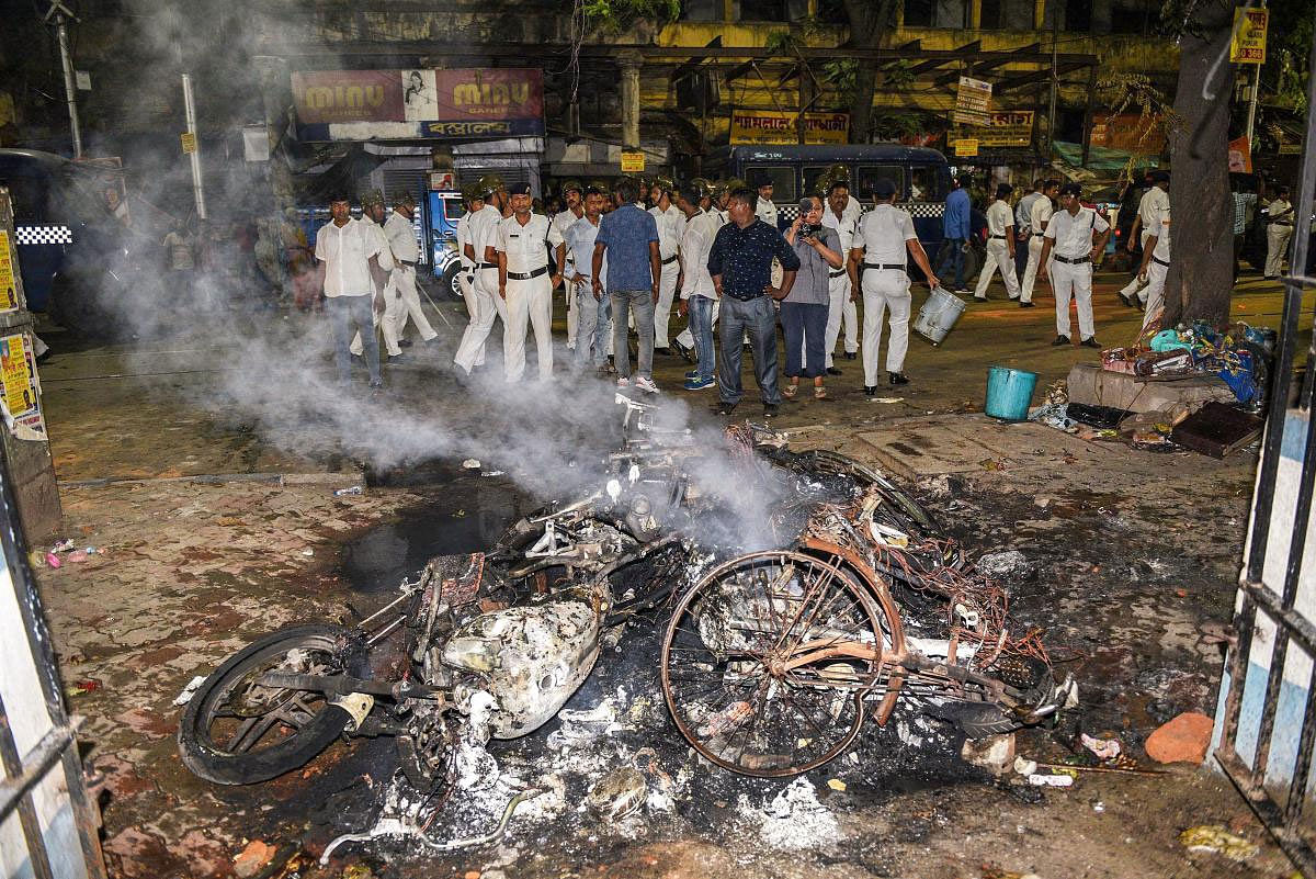 Police personnel look on near vehicles burnt by a mob during BJP President Amit Shah's election roadshow for the last phase of Lok Sabha polls, in Kolkata, Tuesday, May 14, 2019. (PTI Photo)
