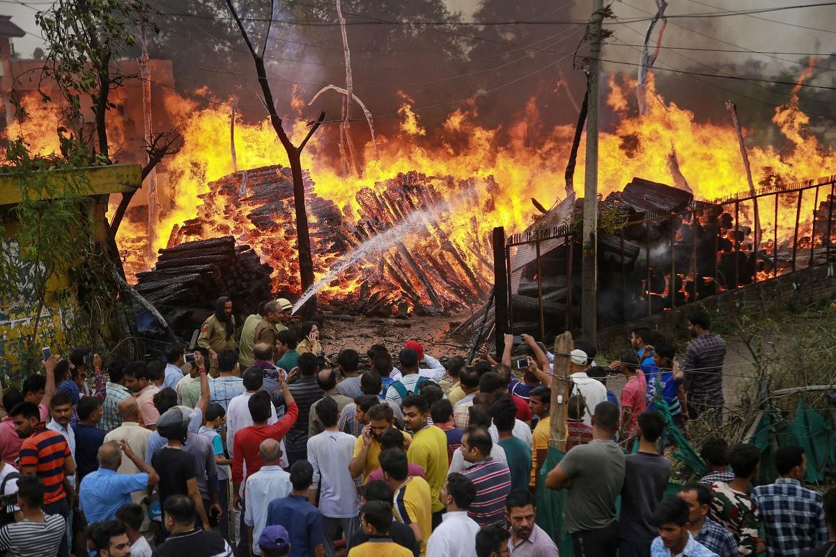 People watch as firefighters douse flames at a timber godown, in Toph Sherkhanian area of Jammu, Tuesday, June 11, 2019. (PTI Photo)