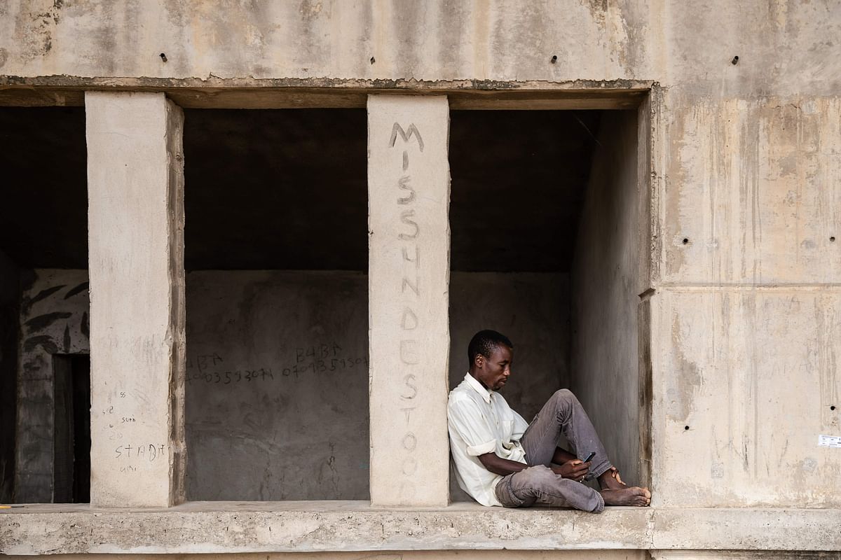 A man pages through his mobile phone while sitting at the Mohammed Goni Stadium internally displaced camp in Maiduguri, north-east Nigeria. (AFP)