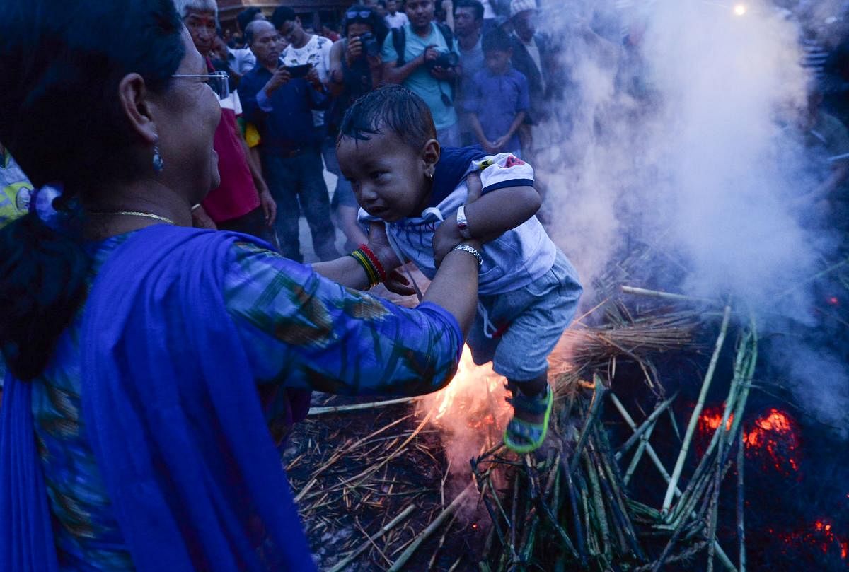 A Nepali devotee carries her child around a fire where a straw effigy of Ghanta Karna will be set alight during celebrations to mark the Hindu festival of