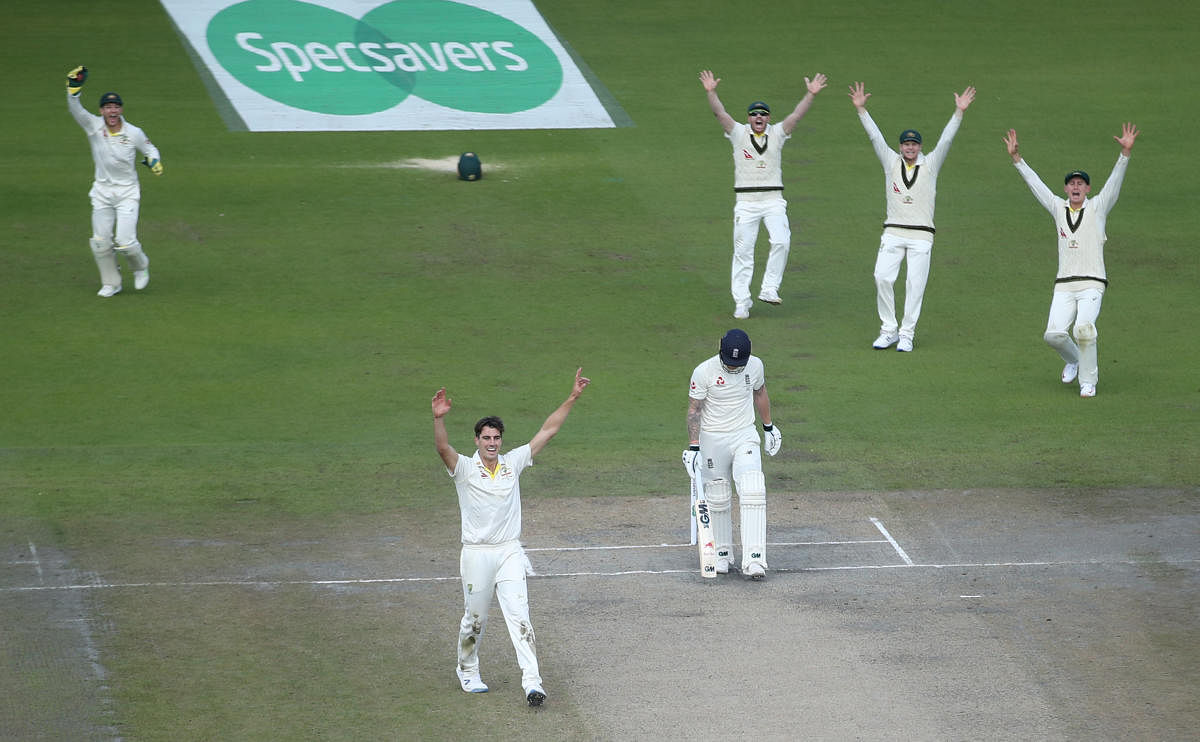 Australia's Pat Cummins and team mates celebrate taking the wicket of England's Ben Stokes who walks off the pitch dejected. (Photo by Reuters)