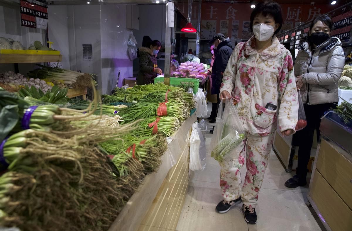 A woman wearing a mask and pajamas shop for vegetables at a store in Beijing, China. (AP Photo)
