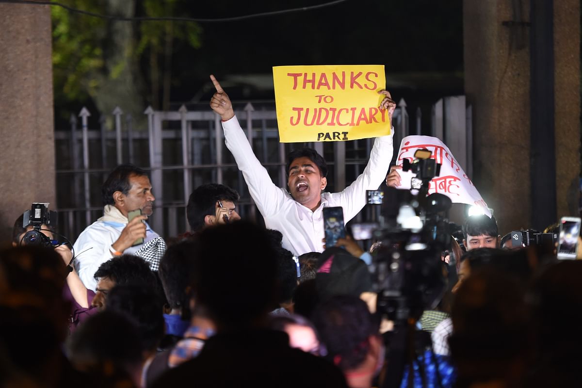 A man holds a placard and shout slogans outside the gates of Tihar Jail after the execution of four men convicted in the gang-rape and murder of a student in 2012. (Credit: AFP)