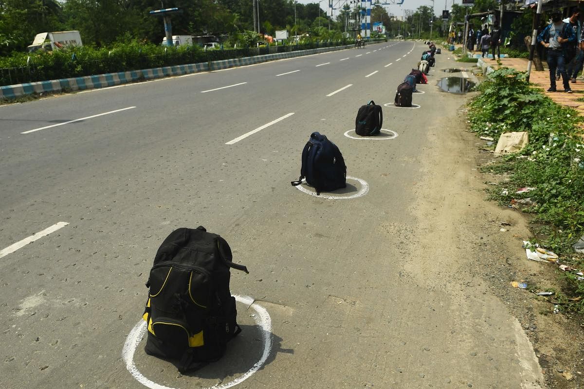 Migrant labourers wait on the shade near their bags placed inside circles marked along a road to maintain social distancing as they wait to board the specially arranged government bus to return to their homes during a government-imposed nationwide lockdown as a preventive measure against the COVID-19 coronavirus, in Kolkata on April 29, 2020. (Photo by Dibyangshu SARKAR / AFP)