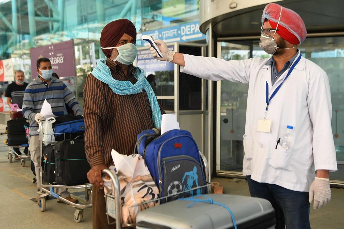 A health worker checks the body temperature of a British national queueing before checking-in for a special flight to London at the Sri Guru Ram Dass jee International Airport on the outskirts of Amritsar