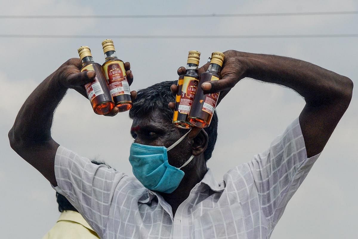 A man gestures as he shows bottles of alcohol bought from a liquor shop after the government eased a nationwide lockdown imposed as a preventive measure against the COVID-19 coronavirus, on the outskirts of Chennai on May 7, 2020. (Photo by Arun SANKAR / AFP)