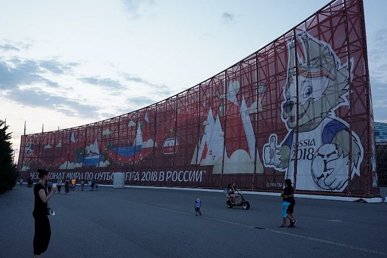People walk past a huge World Cup 2018-themed banner decorated with an image of Zabivaka, the mascot for the football tournament, in Sochi on June 22, 2017. AFP Photo