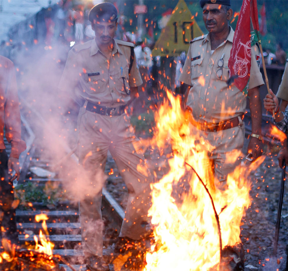 Indian railway policemen stand near a burning effigy representing the Indian government during a protest along railway tracks in Allahabad, India, Thursday, Sept. 20, 2012. Angry opposition workers have disrupted train services as part of a daylong s...