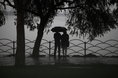 A couple is silhouetted as they stand by a lake sharing an umbrella  during a rain in Hyderabad, India, Monday, July 22, 2013. The annual  monsoon rains which usually hit India from June to September are crucial  for farmers whose crops feed hundreds...