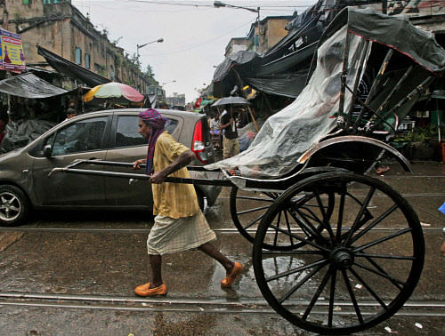 A hand rickshaw puller carries a passenger who takes shelter under a   plastic sheet during rains in Kolkata on Tuesday. PTI Photo