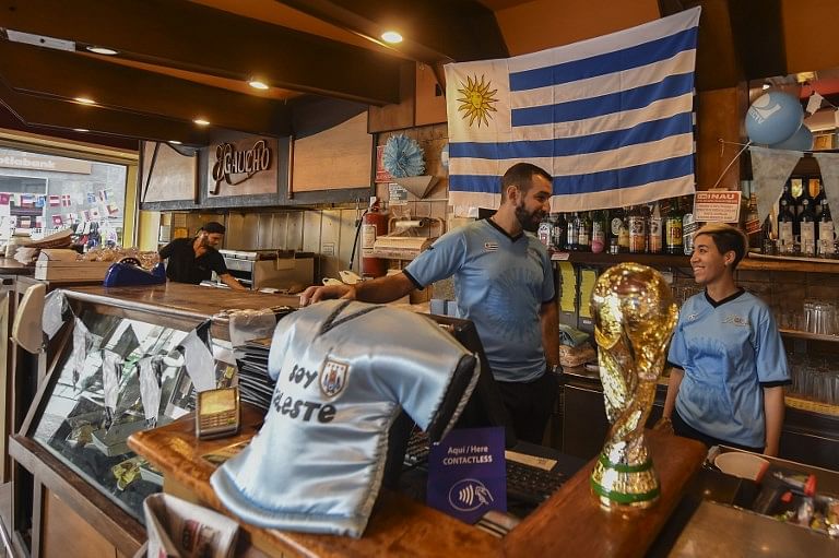 A flag of Uruguay, a replica of the World Cup trophy and a jersey are displayed at a bar in Montevideo in support of the national football team taking part in the FIFA World Cup. The quarter-final match between Uruguay and France is on July 6, 2018. Credit: Miguel ROJO / AFP