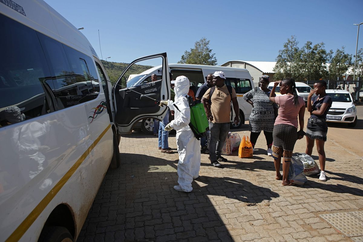 Commuters stand next to a worker contracted by a local insurance company who is spraying disinfectant on a mini-bus taxi in South africa. (Credit: AFP Photo)